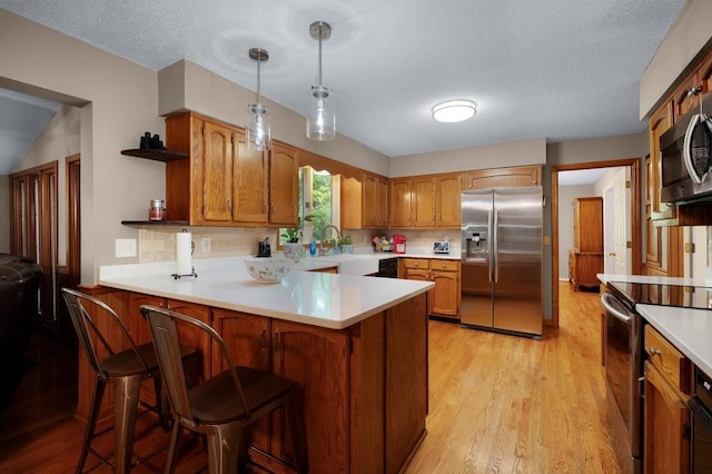 kitchen with light wood-type flooring, hanging light fixtures, kitchen peninsula, and stainless steel appliances