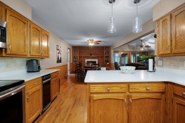 kitchen with light wood-type flooring, kitchen peninsula, hanging light fixtures, backsplash, and appliances with stainless steel finishes