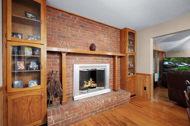 living room featuring built in shelves, wood walls, a textured ceiling, a fireplace, and hardwood / wood-style floors