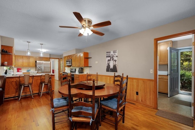 dining space featuring light wood-type flooring, a textured ceiling, wooden walls, and ceiling fan