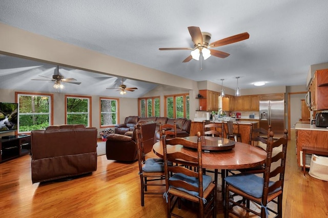 dining space featuring ceiling fan, a textured ceiling, light hardwood / wood-style floors, and vaulted ceiling