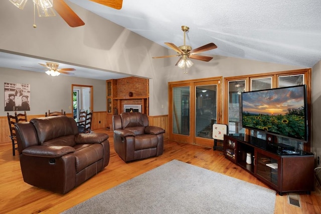 living room featuring ceiling fan, wood walls, hardwood / wood-style floors, a brick fireplace, and vaulted ceiling