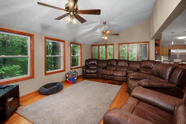 living room with ceiling fan, a textured ceiling, light wood-type flooring, and vaulted ceiling