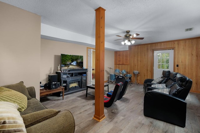 living room with ceiling fan, wooden walls, a fireplace, and light hardwood / wood-style floors