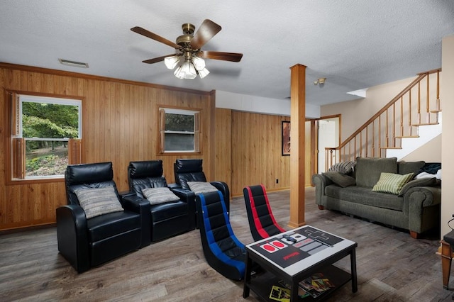 living room with wood-type flooring, a textured ceiling, wood walls, crown molding, and ceiling fan