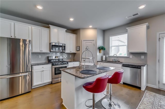 kitchen featuring stainless steel appliances, a sink, visible vents, white cabinetry, and dark stone counters