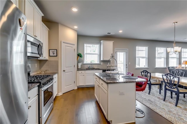 kitchen with a notable chandelier, dark wood-type flooring, white cabinetry, appliances with stainless steel finishes, and a center island with sink