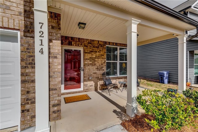 view of exterior entry featuring a porch, brick siding, and an attached garage