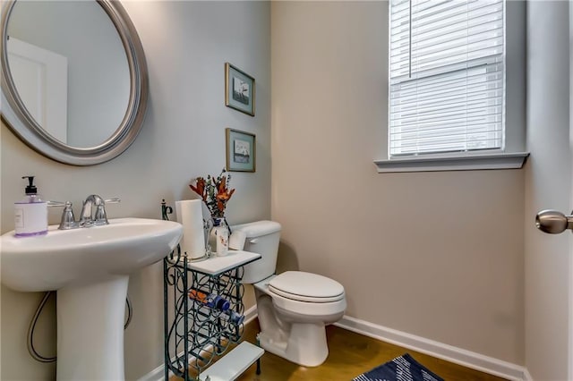 half bathroom featuring toilet, a sink, baseboards, and wood finished floors