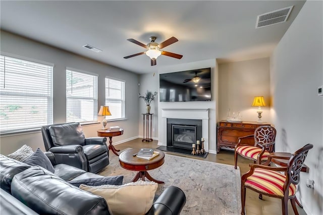 living room with a fireplace with flush hearth, visible vents, baseboards, and a ceiling fan