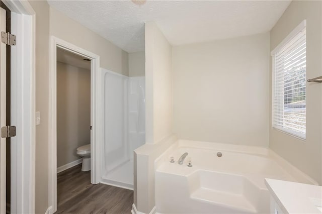 bathroom with wood-type flooring, vanity, toilet, a bath, and a textured ceiling