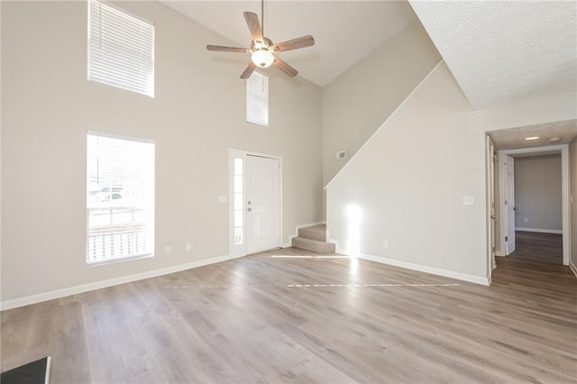 unfurnished living room with ceiling fan, light hardwood / wood-style floors, and a towering ceiling