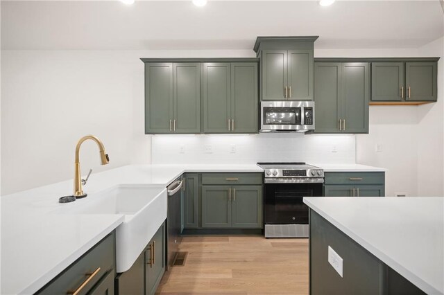 kitchen with sink, green cabinetry, decorative backsplash, light hardwood / wood-style floors, and stainless steel appliances