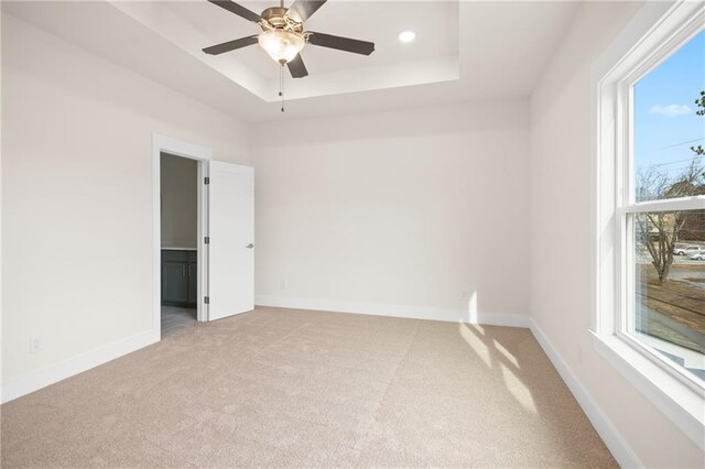 empty room featuring light carpet, a raised ceiling, and ceiling fan