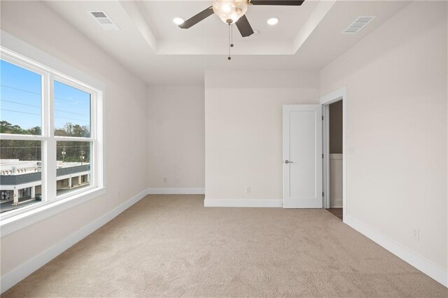 carpeted spare room featuring a raised ceiling and ceiling fan