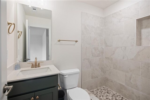 bathroom featuring a tile shower, vanity, and toilet