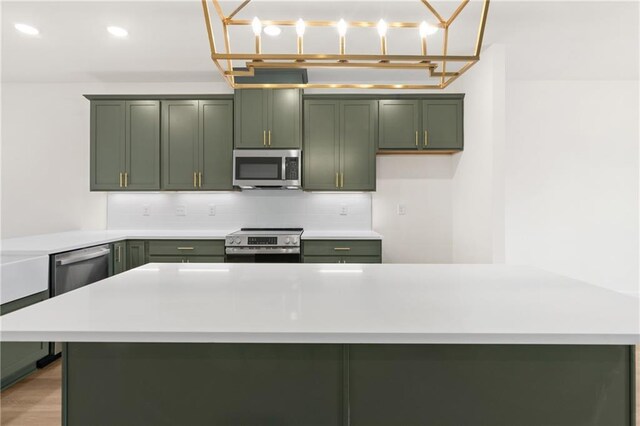 kitchen featuring appliances with stainless steel finishes, light wood-type flooring, backsplash, pendant lighting, and green cabinets