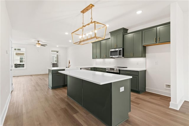 kitchen featuring kitchen peninsula, appliances with stainless steel finishes, ceiling fan with notable chandelier, pendant lighting, and wood-type flooring