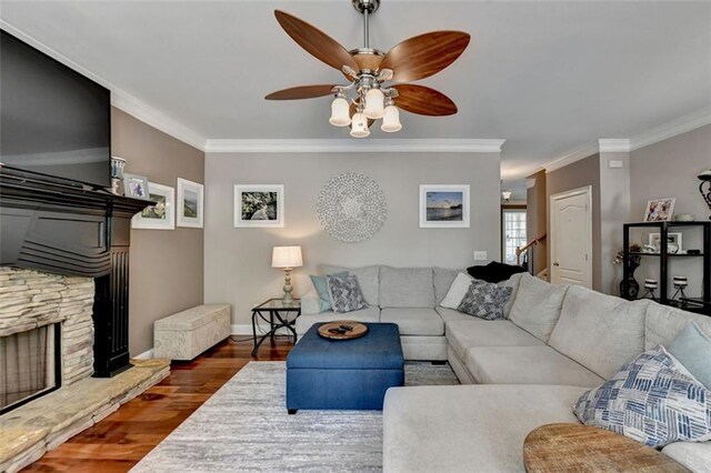 living room with a stone fireplace, ornamental molding, ceiling fan, and dark hardwood / wood-style flooring