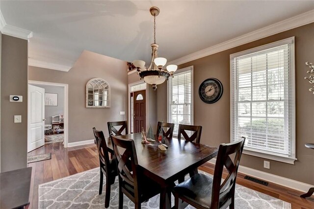 dining area with ornamental molding, a notable chandelier, and hardwood / wood-style floors