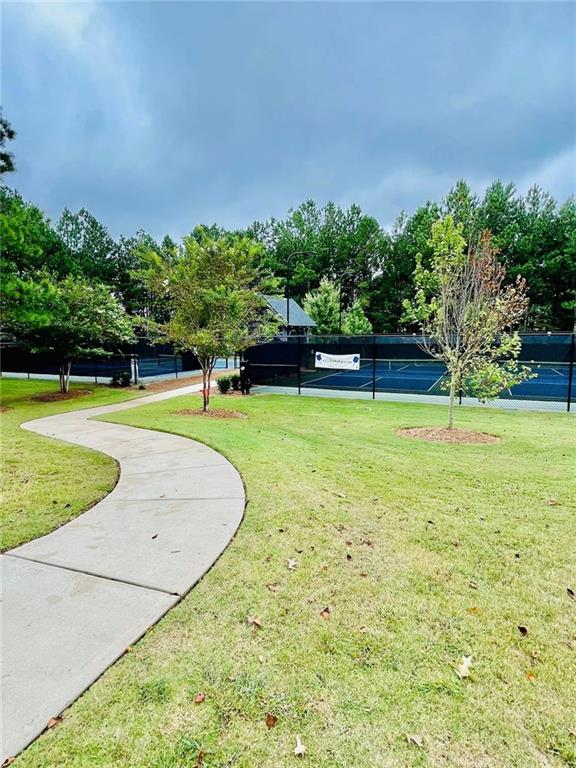 surrounding community featuring a tennis court, fence, and a yard