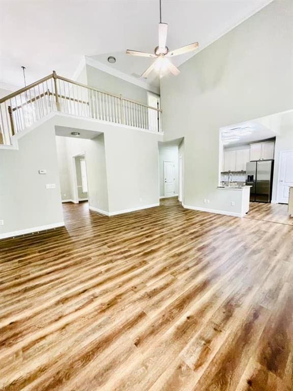 unfurnished living room with ceiling fan, a high ceiling, baseboards, stairway, and light wood-type flooring