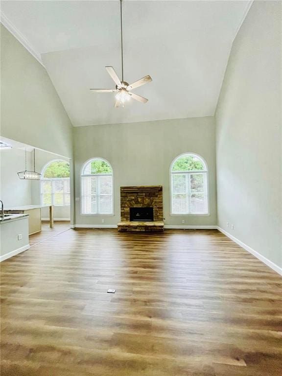 unfurnished living room with a wealth of natural light, high vaulted ceiling, wood finished floors, and a stone fireplace