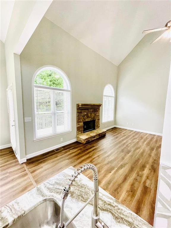 living area featuring a fireplace, high vaulted ceiling, a wealth of natural light, and wood finished floors