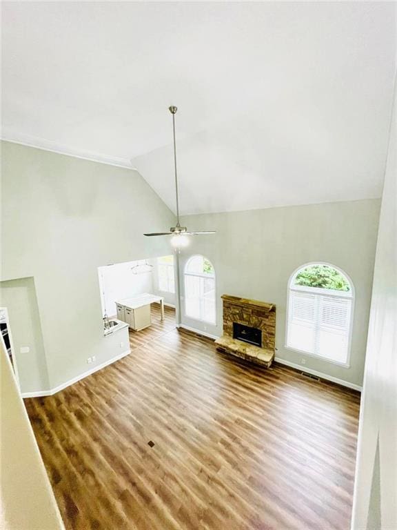 unfurnished living room with a ceiling fan, vaulted ceiling, wood finished floors, and a stone fireplace