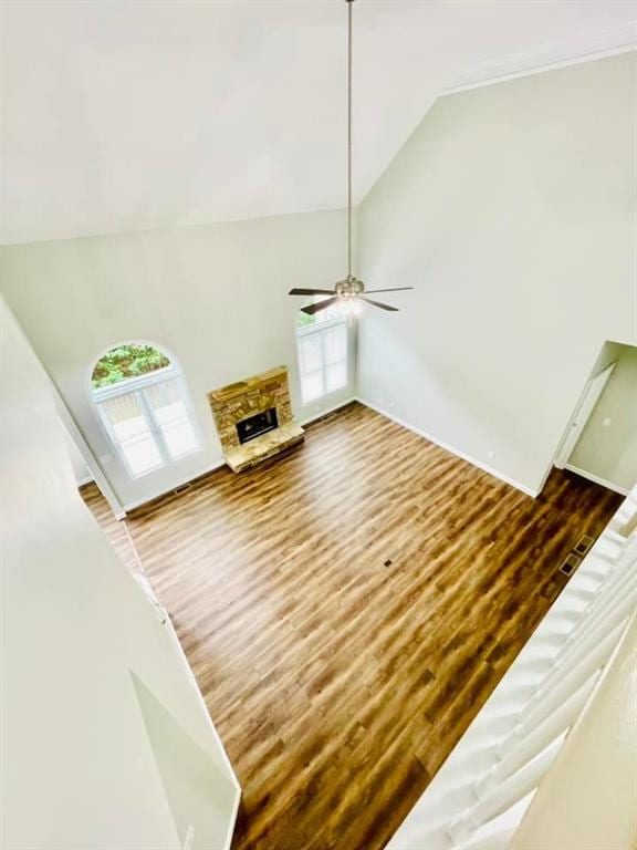 unfurnished living room with a ceiling fan, high vaulted ceiling, wood finished floors, and a stone fireplace