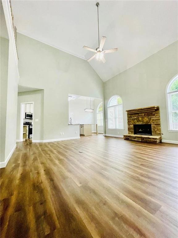 unfurnished living room with a ceiling fan, a stone fireplace, wood finished floors, high vaulted ceiling, and baseboards