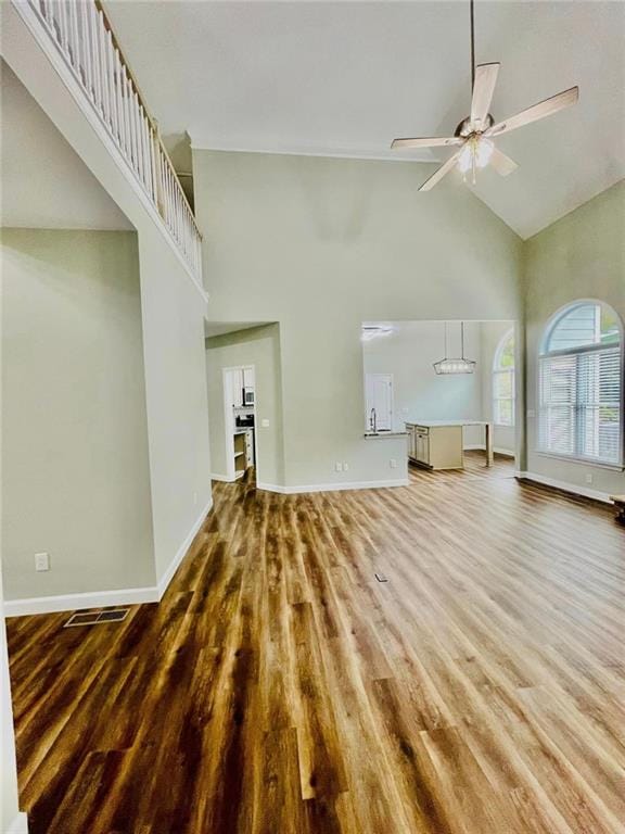 unfurnished living room with baseboards, high vaulted ceiling, ceiling fan, and wood finished floors