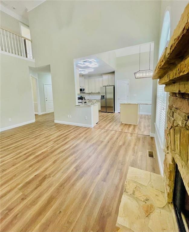 unfurnished living room with light wood-style flooring, a high ceiling, a fireplace, visible vents, and baseboards