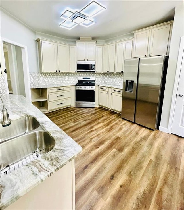 kitchen with stainless steel appliances, a sink, light wood-style floors, backsplash, and light stone countertops