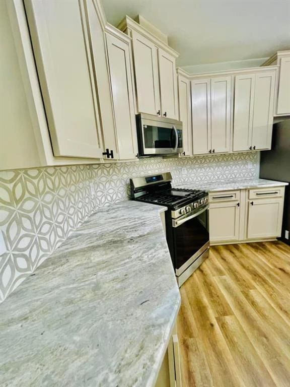 kitchen featuring stainless steel appliances, light wood-style flooring, light stone counters, and tasteful backsplash