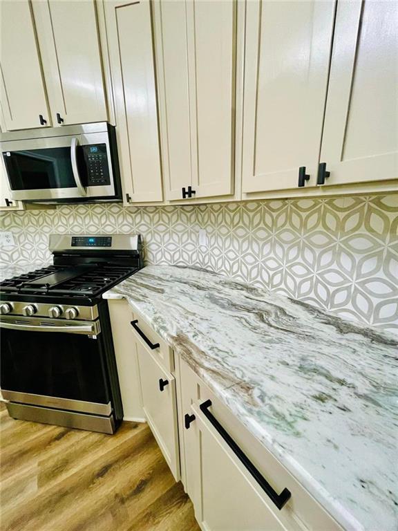 kitchen featuring light wood-style floors, tasteful backsplash, appliances with stainless steel finishes, and light stone counters