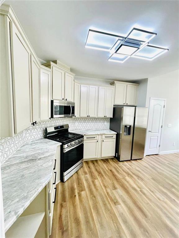 kitchen with stainless steel appliances, backsplash, light wood-style flooring, and white cabinets