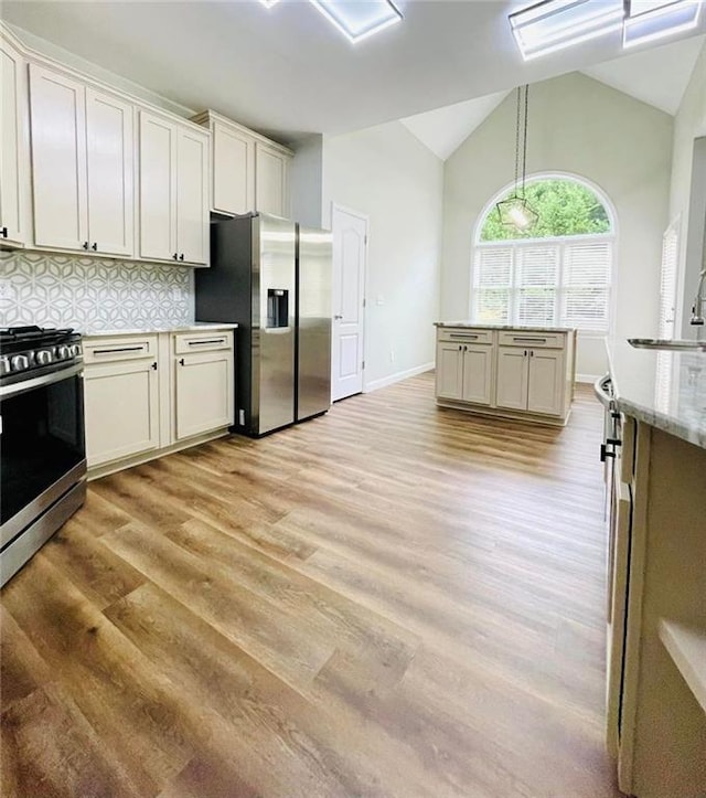 kitchen featuring light stone counters, pendant lighting, stainless steel appliances, tasteful backsplash, and vaulted ceiling