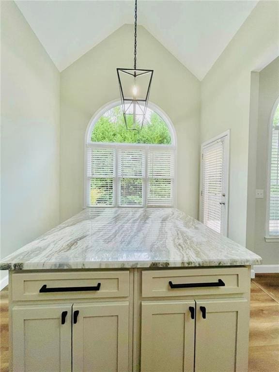 kitchen with pendant lighting, cream cabinets, a kitchen island, vaulted ceiling, and light stone countertops