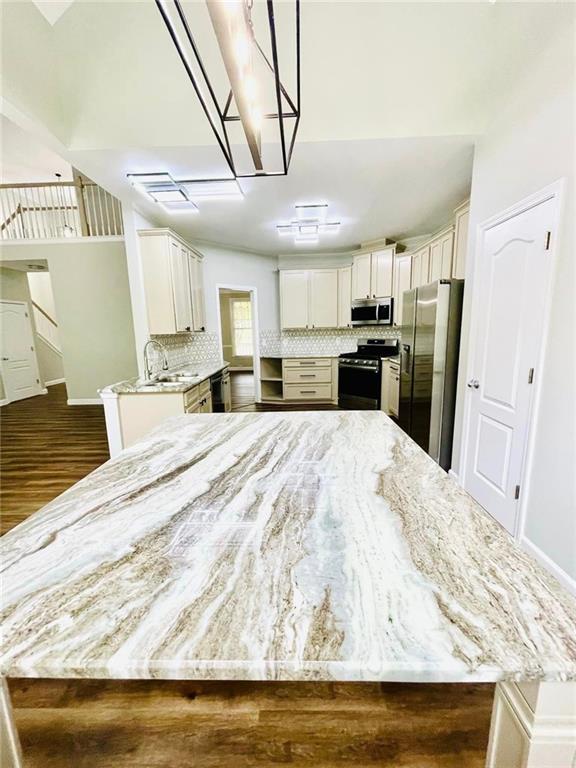 kitchen with tasteful backsplash, white cabinets, appliances with stainless steel finishes, a peninsula, and light stone countertops