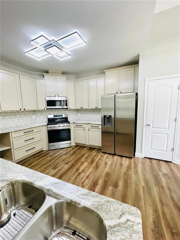 kitchen with light stone counters, stainless steel appliances, tasteful backsplash, cream cabinets, and light wood-style floors