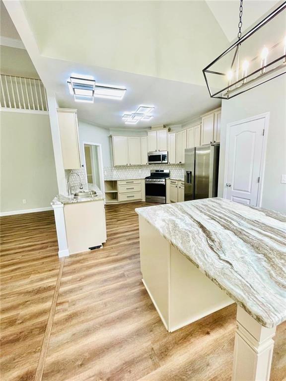 kitchen featuring light stone counters, light wood-style flooring, stainless steel appliances, white cabinets, and decorative light fixtures