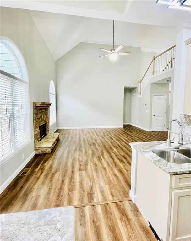 unfurnished living room with light wood finished floors, a ceiling fan, a sink, a stone fireplace, and high vaulted ceiling