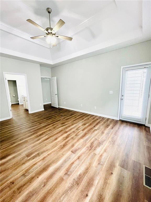 unfurnished bedroom featuring ceiling fan, visible vents, baseboards, light wood-type flooring, and a raised ceiling