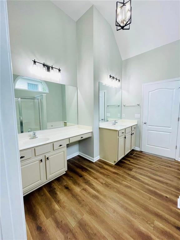 bathroom featuring two vanities, wood finished floors, a shower stall, high vaulted ceiling, and a sink