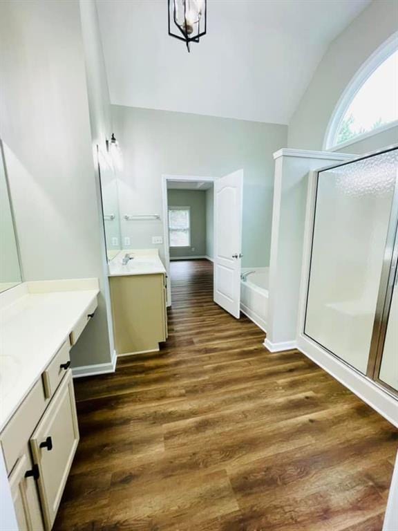 full bathroom with a stall shower, lofted ceiling, two vanities, wood finished floors, and a bath