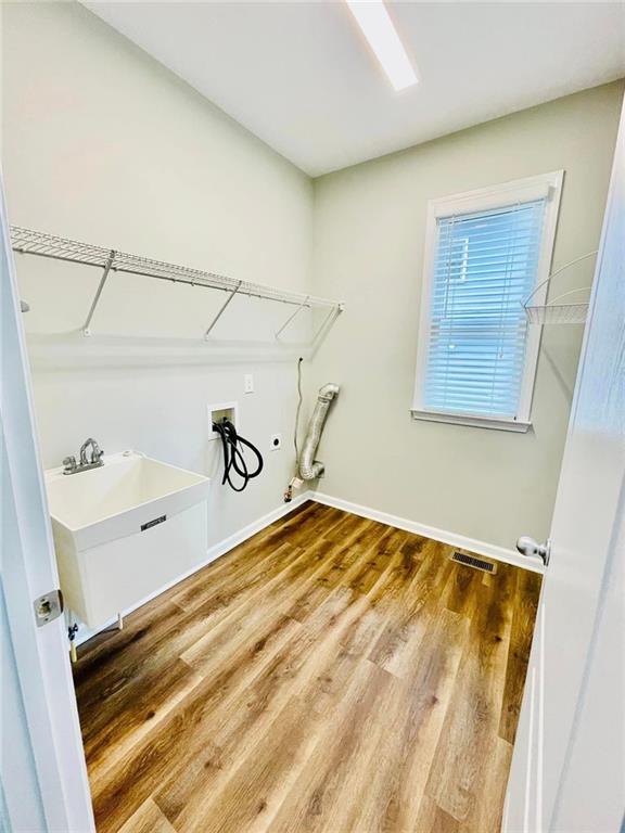 clothes washing area with laundry area, visible vents, baseboards, wood finished floors, and washer hookup