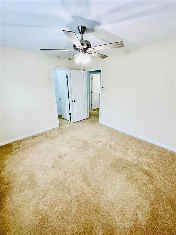 empty room with a ceiling fan, light carpet, and baseboards