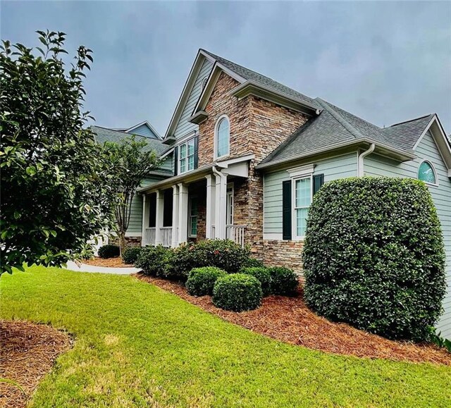 view of front of home with stone siding, a shingled roof, and a front lawn