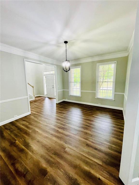 spare room featuring dark wood-style floors, a chandelier, crown molding, and baseboards